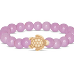 A beaded stretch Fahlo bracelet featuring smooth, round lilac glow beads and a carved natural turtle charm in the center, displayed on a clean white background. Available at Be Charmed