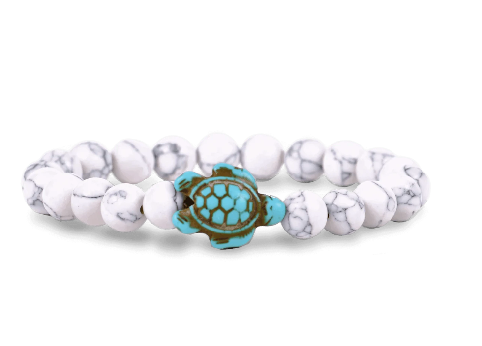 A beaded stretch Fahlo bracelet featuring white and white marbled round beads with a central turquoise and brown turtle charm, shown on a plain white background. Available at Be Charmed