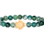 A beaded stretch Fahlo bracelet featuring round seagrass green marbled beads with a central cream-colored turtle charm, shown on a plain white background. Available at Be Charmed