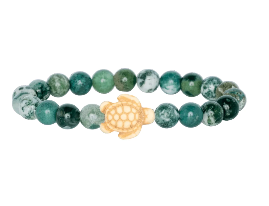 A beaded stretch Fahlo bracelet featuring round seagrass green marbled beads with a central cream-colored turtle charm, shown on a plain white background. Available at Be Charmed