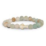 A beaded stretch Fahlo bracelet featuring natural stone beads in muted shades of green, beige, and brown, with a small whale shark  at the center, shown on a plain white background. Available at Be Charmed
