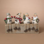 Four Christmas-themed resin figurines sitting on a weathered wooden block against a solid beige background. The set includes two snowmen and two Santa Claus figures, each with painted white bodies, colorful scarves and hats, and dark brown boots. Availabe at Be Charmed