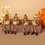 Four small decorative bird figurines dressed in autumn clothing, seated on a wooden block against a warm beige background with floral props on both sides. Available at Be Charmed