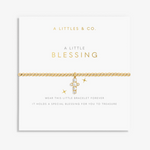 A gold chain bracelet with a small cross charm and clear stones, displayed on a white branded card that reads 'A LITTLES & CO. A LITTLE BLESSING'. Available at Be Charmed