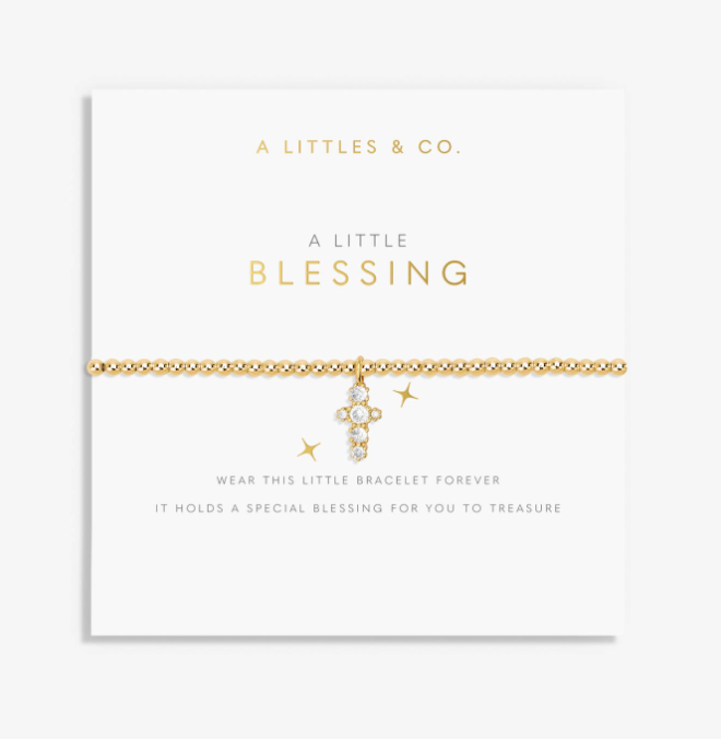 A gold chain bracelet with a small cross charm and clear stones, displayed on a white branded card that reads 'A LITTLES & CO. A LITTLE BLESSING'. Available at Be Charmed