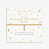A gold celestial-themed bracelet by A Littles & Co. displayed on its white backing card, which features gold stars, moons, and text reading 'A LITTLE MAGICAL BIRTHDAY WISH'. Available at Be Charmed