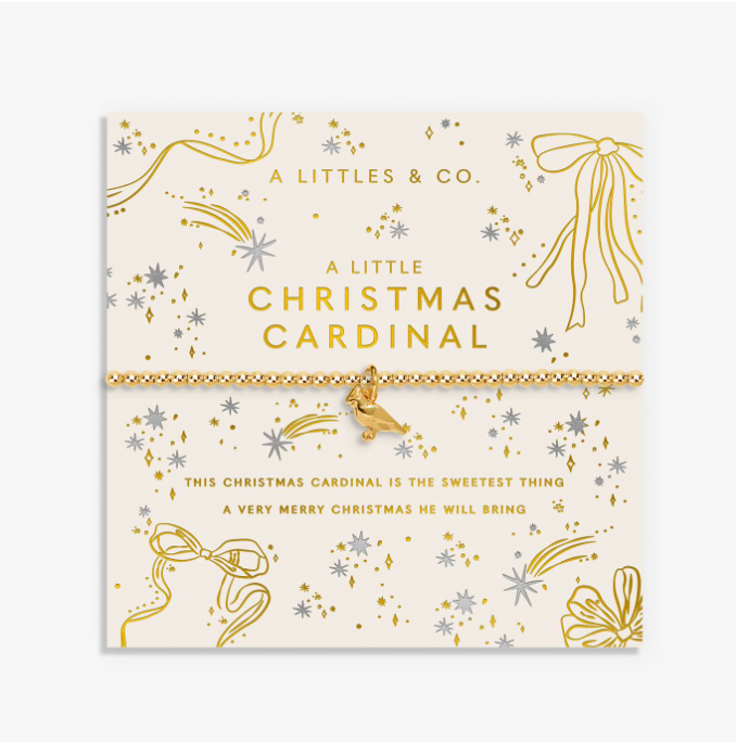 A Little Christmas Cardinal bracelet by A Little's & Co. displayed on its cream-colored illustrated card packaging, featuring gold and silver glittery details and a small gold bird charm. Available at Be Charmed