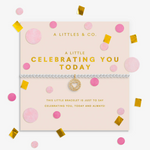 A silver-toned bracelet with a gold star charm and a delicate chain, presented on a light pink branded card. The card is decorated with pink circles, gold confetti, and gold foil text reading 'A LITTLES & CO. Available at Be Charmed