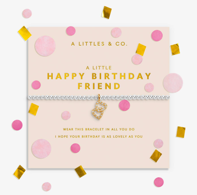 A silver-toned bracelet with a gold heart charm and rhinestone trim, presented on a pale pink card that reads 'A LITTLE HAPPY BIRTHDAY FRIEND.' The card is surrounded by pink and gold confetti on a white background. Available at Be Charmed