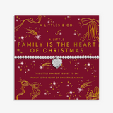 A silver heart-shaped charm bracelet by A Littles & Co. displayed on its red and gold Christmas-themed gift card, which reads 'A LITTLE FAMILY IS THE HEART OF CHRISTMAS'. Available at Be charmed
