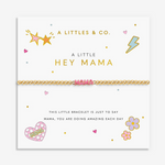 A gold chain bracelet with a pink heart-shaped charm spelling 'MAMA' is displayed on a white gift card. The card features gold and pink decorative illustrations including stars, hearts, flowers, and text that reads 'A LITTLES & CO. Available at Be Charmed