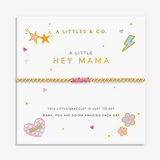 A gold chain bracelet with a pink heart-shaped charm spelling 'MAMA' is displayed on a white gift card. The card features gold and pink decorative illustrations including stars, hearts, flowers, and text that reads 'A LITTLES & CO. Available at Be Charmed