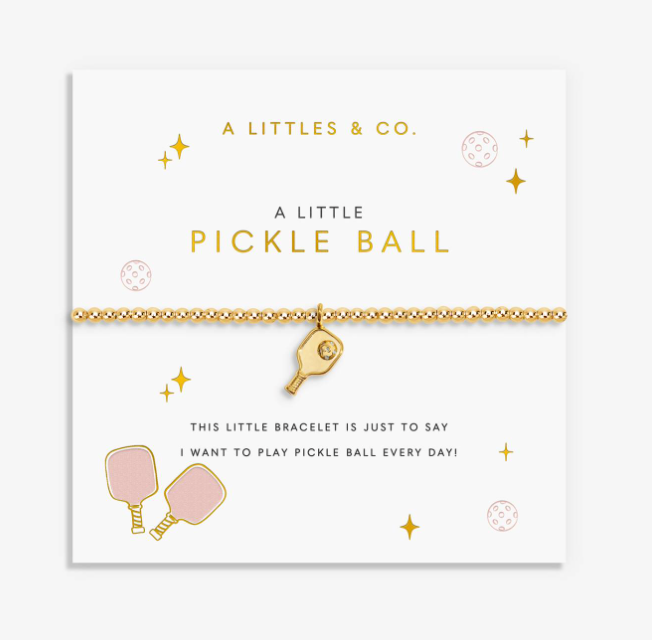 A gold pickleball bracelet by A Littles & Co. on a white gift card with gold and pink text and illustrations, featuring a small pickleball paddle charm. Available at Be Charmed
