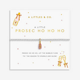 A silver-toned bracelet with a pink and gold 'Prosecco' pendant, displayed on a white branded card from 'A Littles & Co.' with champagne bottle and glasses illustrations. Available at Be Charmed