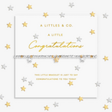 A silver and gold beaded bracelet with star charms, presented on a white card from A Littles & Co. with gold and silver star confetti scattered around the background. Available at Be Charmed