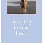 A greeting card featuring an image of a dog on the beach with the text 'carry joy in your heart' printed on it. Available at Be Charmed