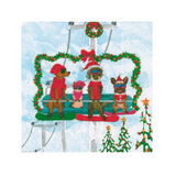A Caspari square printed napkin or paper product featuring a festive winter scene with four dogs on a ski lift chair, decorated with green wreaths and red holiday accents, set against a snowy blue background. Available at Be Charmed
