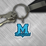 A clear acrylic keychain with a metal ring, featuring a blue 'M' logo that reads 'MEDFIELD', attached to a black keychain clip. Available at Be Charmed