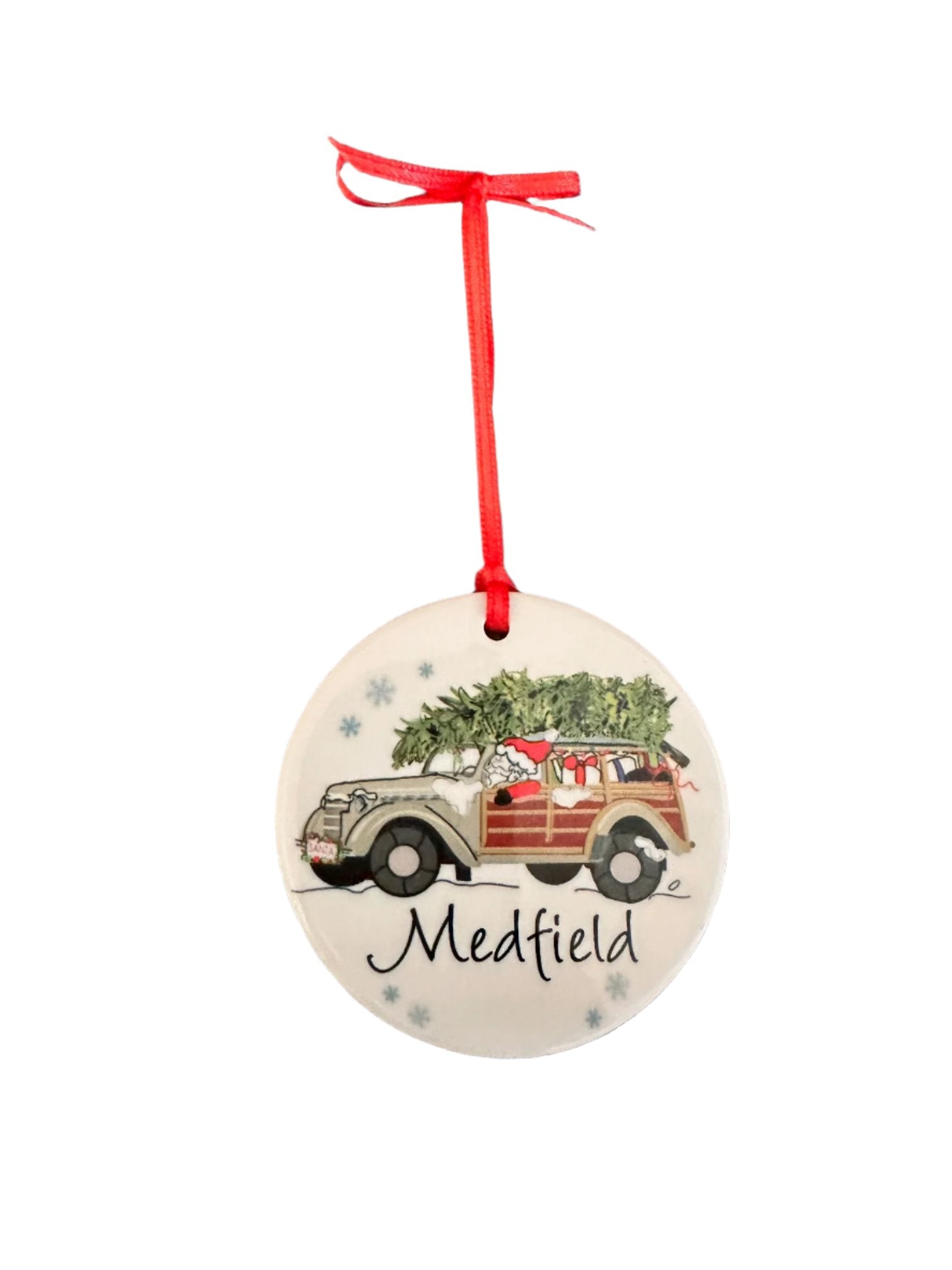 A round ceramic ornament featuring a depiction of Santa Claus in a woodie vehicle with the text 'MEDFIELD' on the side, hanging from a red ribbon. Available at Be Charmed
