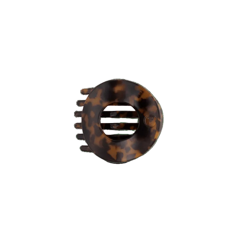 A circular hair claw clip in a classic tortoiseshell pattern, featuring a central ventilation slot and five outer teeth, shown on a plain white background. Available at Be Charmed