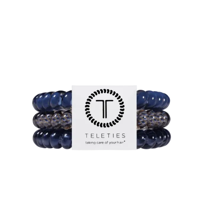 Three Teleties hair stretch bands in navy blue and clear patterned material, wrapped around a white paper band with the Teleties logo and name. Avaialbe at Be Chamred