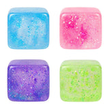 Four colorful glittery cubes in blue, pink, purple, and green on a white background. Available at Be Charmed