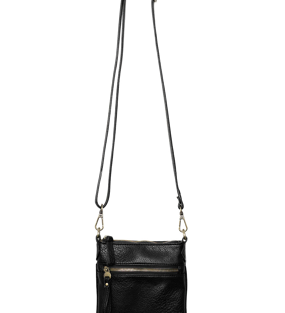 A Joy Susan Lia black pebbled crossbody bag with a long shoulder strap, hanging from a wooden peg against a solid white background. Available at Be Charmed
