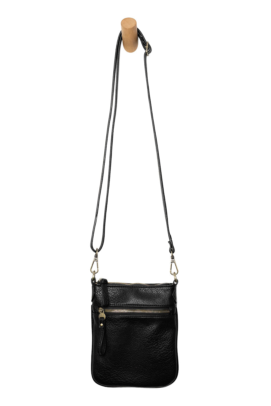 A Joy Susan Lia black pebbled crossbody bag with a long shoulder strap, hanging from a wooden peg against a solid white background. Available at Be Charmed