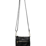 A Joy Susan Lia black pebbled crossbody bag with a long shoulder strap, hanging from a wooden peg against a solid white background. Available at Be Charmed