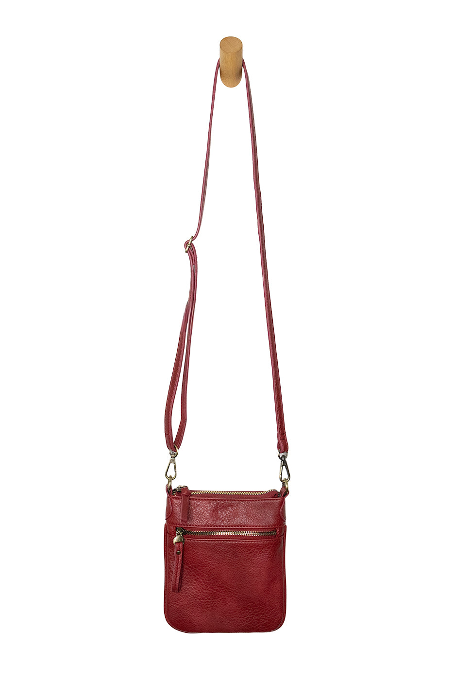 A Joy Susan Lia chilli crossbody bag with a long adjustable strap, hanging from a wooden peg against a plain white background. Available at Be Charmed