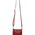 A Joy Susan Lia chilli crossbody bag with a long adjustable strap, hanging from a wooden peg against a plain white background. Available at Be Charmed