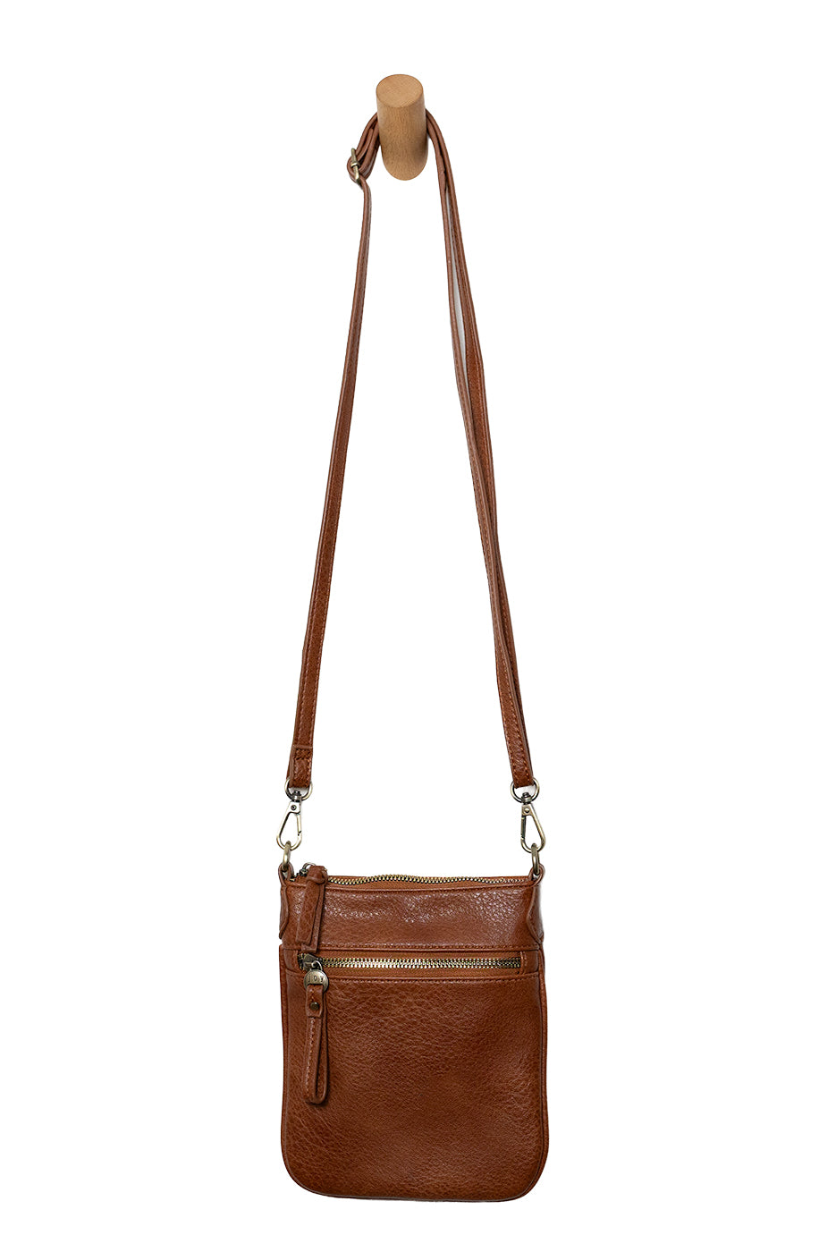 A Joy Susan cognac Lia crossbody bag with a long adjustable strap, hanging from a wooden peg on a white background. Available at Be Charmed