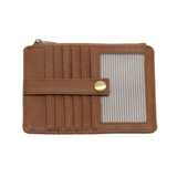 A Joy Susan pecan card holder wallet with multiple card slots, a horizontal strap with a gold snap button, and a clear striped ID window on the front, shown against a plain white background. Available at Be Charmed