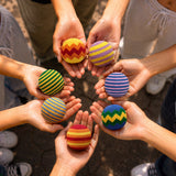Hands holding colorful striped balls in a circle. Available at Be Charmed