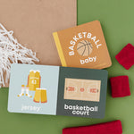 Basketball-themed baby items including a book, cards, and headbands on a green background. Availabe at Be Charmed