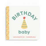 A baby picture book titled 'BIRTHDAY baby' by Danielle Wilson, featuring a cream-colored cover with a yellow party hat illustration and a yellow spine decorated with multicolored sprinkles. Available at Be Charmed