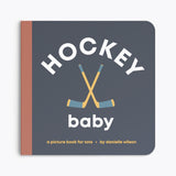 Book titled 'Hockey Baby' with hockey sticks on a dark blue background. Available at Be Charmed
