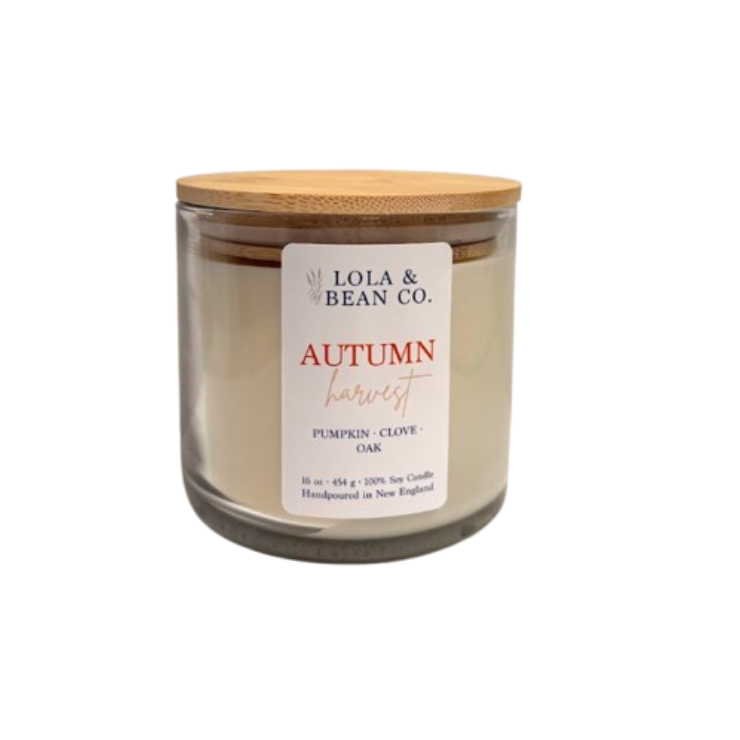A 16 oz soy candle in a clear glass jar with a light wood lid, featuring a white label that reads 'Lola & Bean Co. Autumn Harvest Pumpkin-Clove Oak'. Available at Be Charmed