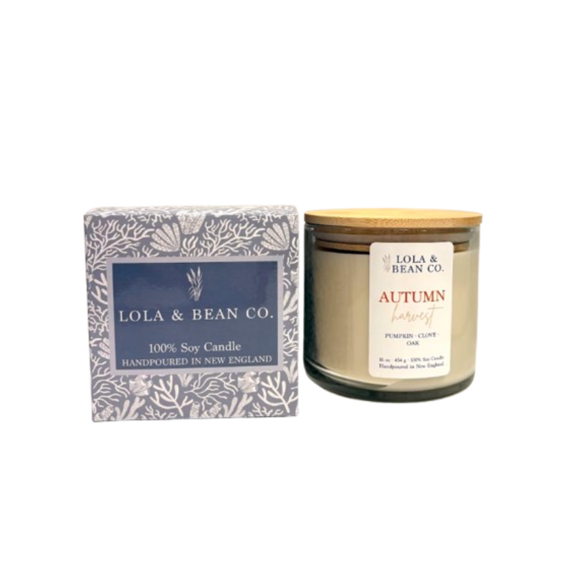 Lola & Bean Co. Autumn Harvest handpoured soy candle in a clear glass jar with a light wood lid, shown next to its patterned blue and white packaging box on a white background. Available at Be Charmed