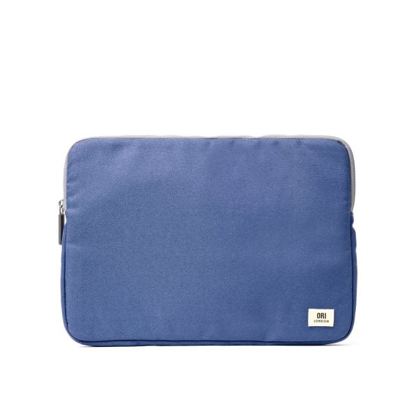 A blue Ori fabric laptop sleeve with a small white brand tag on the bottom right corner, shown against a plain white background. Available at Be Charmed