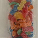 A clear plastic bag filled with assorted colorful sour gummy candies, photographed from above on a plain white surface. Available at Be Charmed