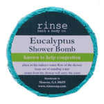 A circular blue shower bomb packaging with a label that reads 'Eucalyptus Shower Bomb' from Rinse Bath & Body Co. Available at Be Charmed
