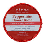 A circular blue shower bomb packaging with a label that reads 'Peppermint Shower Bomb' from Rinse Bath & Body Co. Available at Be Charmed