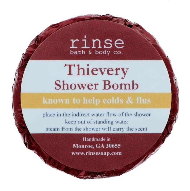 A circular blue shower bomb packaging with a label that reads 'Thievery Shower Bomb' from Rinse Bath & Body Co. Available at Be Charmed