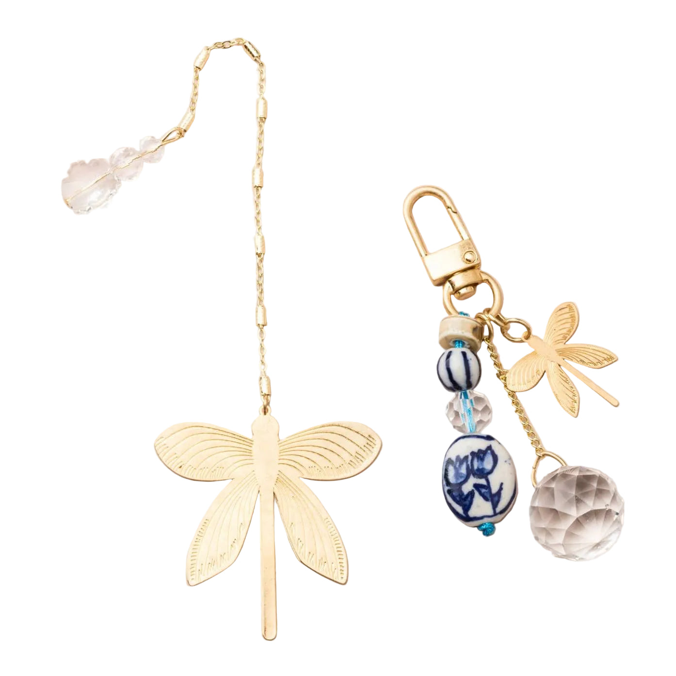 A gold dragonfly bookmark with a long chain and clear crystal bead, displayed next to a matching gold dragonfly keychain charm with blue and white patterned beads, a faceted clear crystal, and a gold clasp on a light pink background. Available at Be Charmed