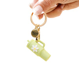 A green colored tumbler keychain with a flower detail on a white background, attached to a keyring. Available at Be Charmed