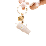 A oat colored tumbler keychain with a flower detail on a white background, attached to a keyring. Available at Be Charmed