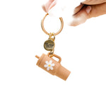 A sandstone colored tumbler keychain with a flower detail on a white background, attached to a keyring. Available at Be Charmed