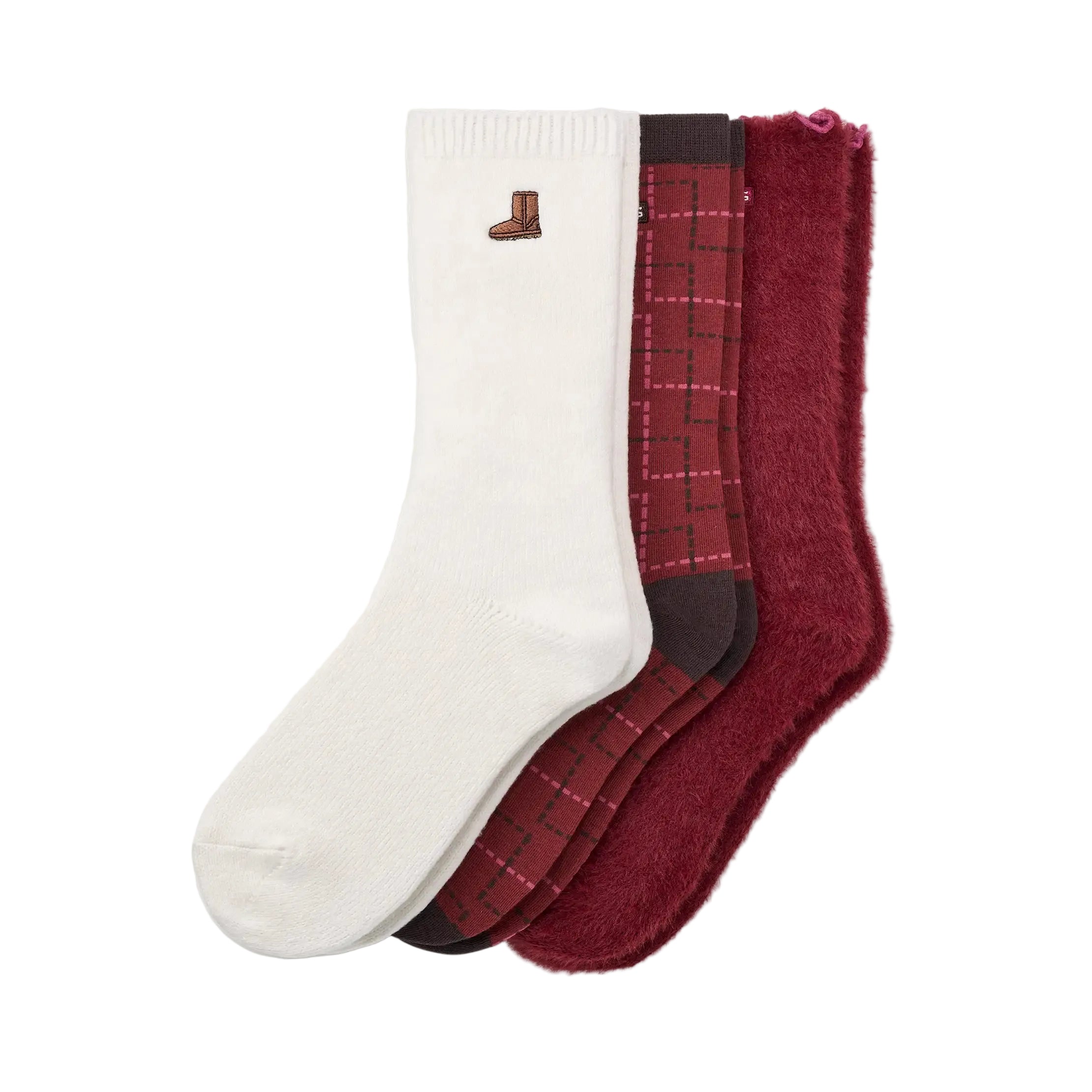 Three pairs of UGG crew socks arranged overlapping on a light off-white background: one white sock with a small brown boot logo near the cuff, one dark red plaid sock, and one plush deep burgundy sock. Available at Be Charmed