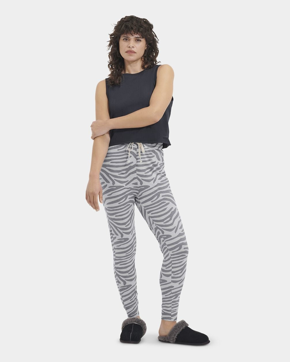 A woman standing, wearing high-waisted drawstring pants with a cloudy grey and white stripe pattern, paired with a black top and black footwear. Available at Be Charmed